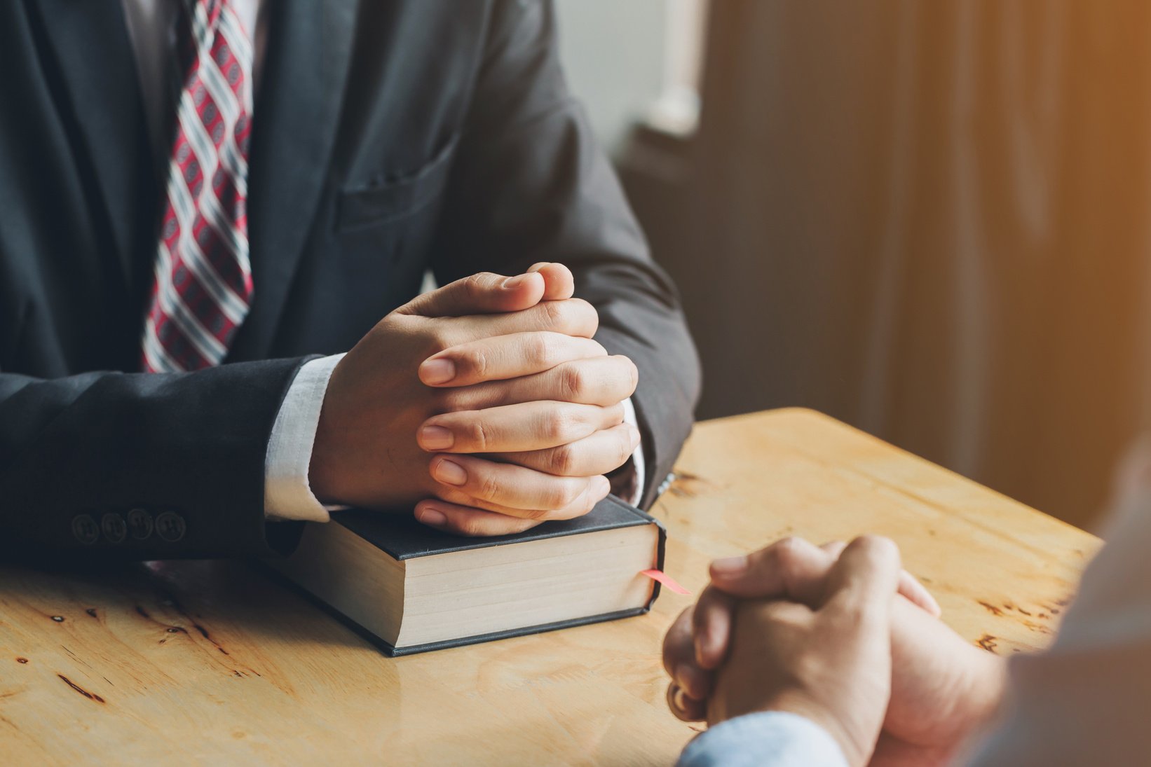 Two People Praying Together over Holy Bible on Wooden Table